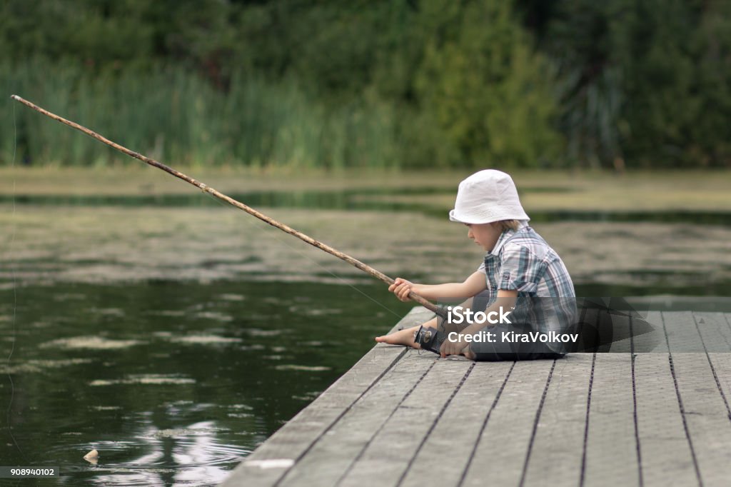 Little boy with old-fashioned fishing rod on a wooden pier Fishing Stock Photo