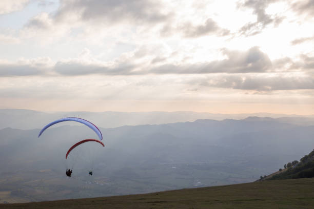 Photo of Some colorful paragliders flying over a mountain scenery, with some faint sunrays in the background