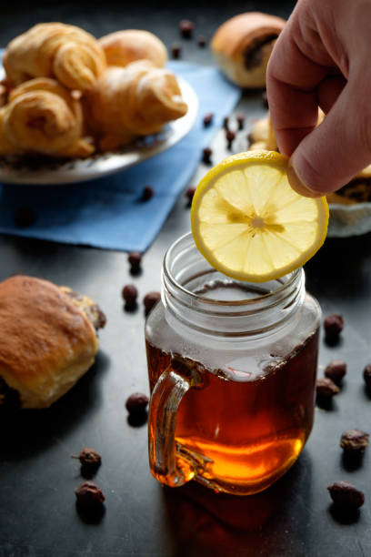 istock man's hand putting lemon slice in jar cup filled with black tea, buisquits on back front 908948560