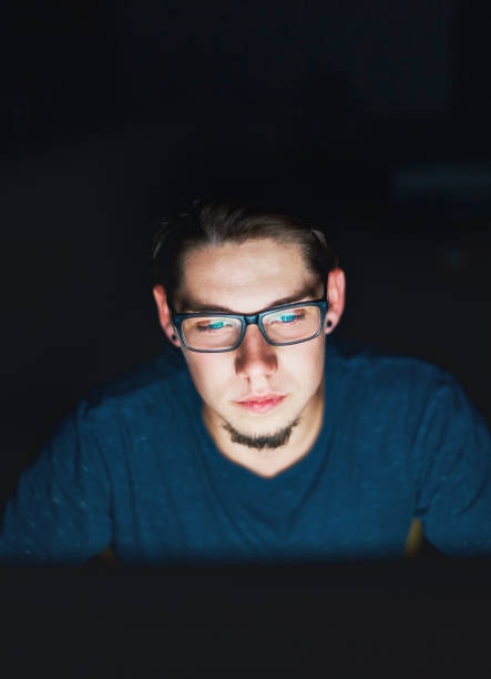 istock Serious young man wearing glasses works on computer by night 908952954