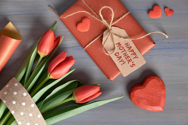 Wrapped gift red tulips, wrapping paper and decorative hearts on wooden table