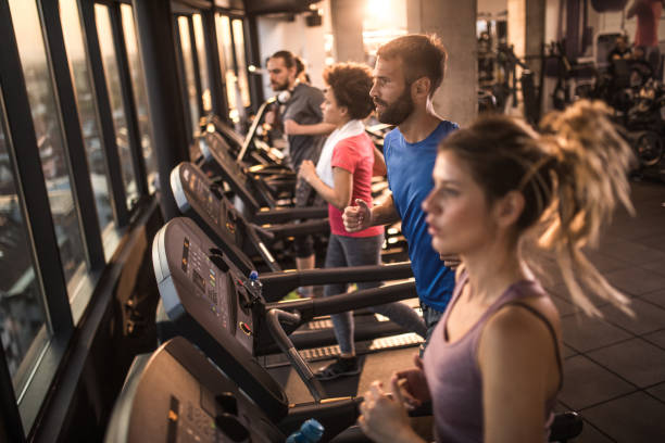 istock Young athletic people warming up while jogging on treadmills in a gym. 908953782