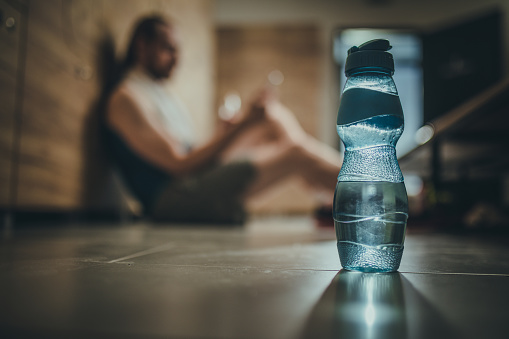 Close up of bottle with fresh water at gym's dressing room with an athlete in the background.