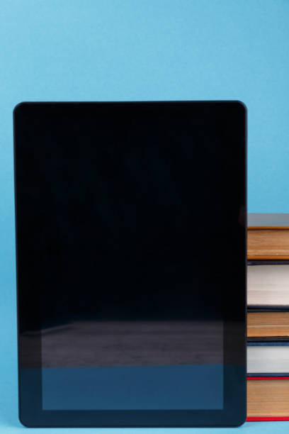 istock A black tablet is next to a stack of books. Close-up. On a blue background. 908964142