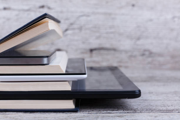 Various tablets are among a stack of books. On a wooden background. Close-up.