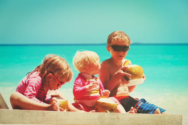 istock little boy and two girls drinking coconut on beach 908969258