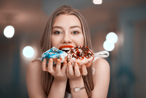 front view of cute woman laughing and eating delicious donuts, lifestyle shot.