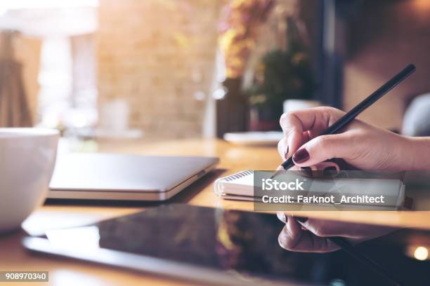 Closeup Image Of Womans Hand Writing On A Blank Notebook With Laptop Tablet And Coffee Cup On Wooden Table Background Stock Photo - Download Image Now