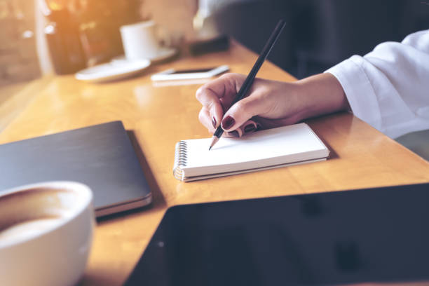 istock Closeup image of woman's hand writing on a blank notebook with laptop , tablet and coffee cup on wooden table background 908970398