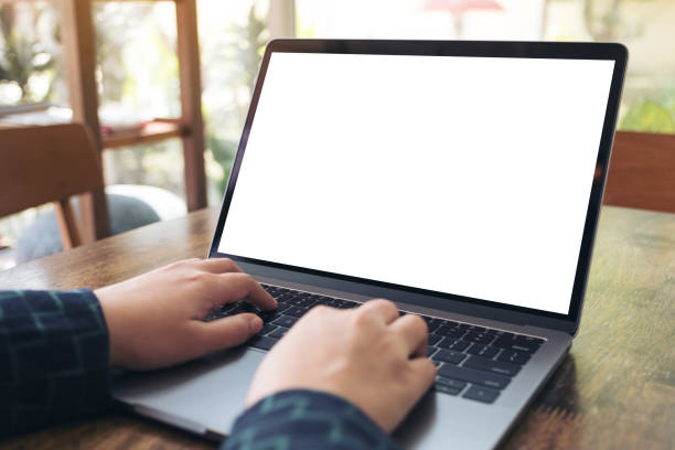 istock Mockup image of hands using and typing on laptop with blank white desktop screen on wooden table in cafe 908971272