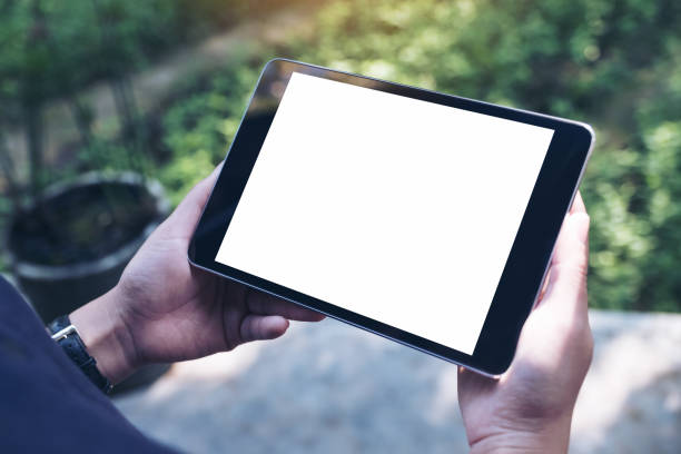 istock Mockup image of woman's hands holding black tablet pc with blank white screen and green nature background 908971274