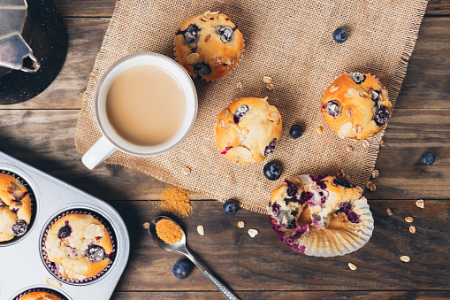 Freshly baked blueberry muffins with almond, oats and icing sugar topping on a rustic wooden table and a mug of coffee. Top view,