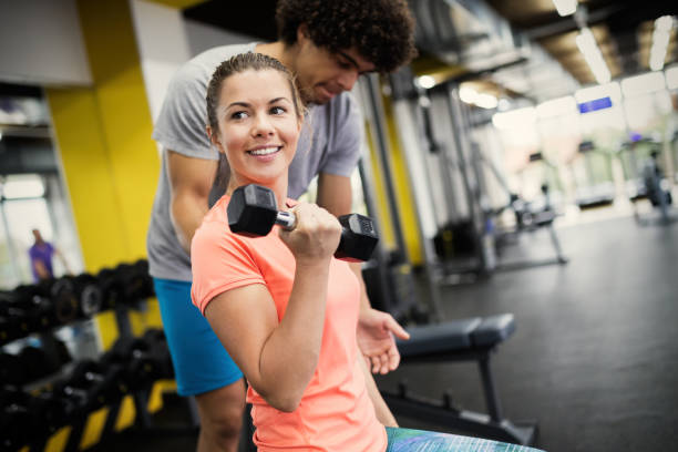 istock Beautiful woman doing exercises in gym with personal trainer 908985558