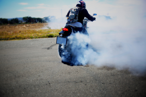 Biker does a donut on a road, causing smoke on the asphalt