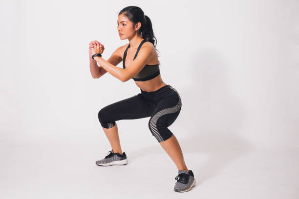 Young sporty muscular woman doing squats isolated over white background. Woman in sport clothing performing exercise Young sporty muscular woman doing squats isolated over white background. Woman in sport clothing performing exerciseYoung sporty muscular woman doing squats isolated over white background. Woman in sport clothing performing exercise squatting position photos stock pictures, royalty-free photos & images