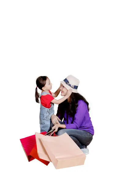 Portrait of young mother squatting with her daughter and holding shopping bags in the studio