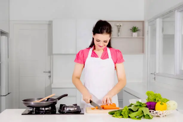 Picture of beautiful woman cutting a carrot while cooking in the kitchen