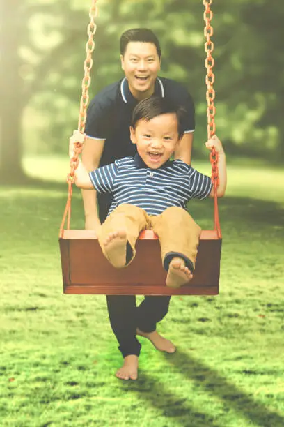 Image of Happy father and his son playing with a swing while having fun together in the park