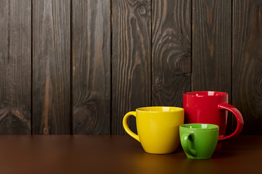 Different in size and color ceramic cups for coffee and tea - red, yellow and green on a dark wooden background. Selective focus.