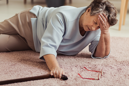 Sick senior woman with headache lying on the floor with wooden stick