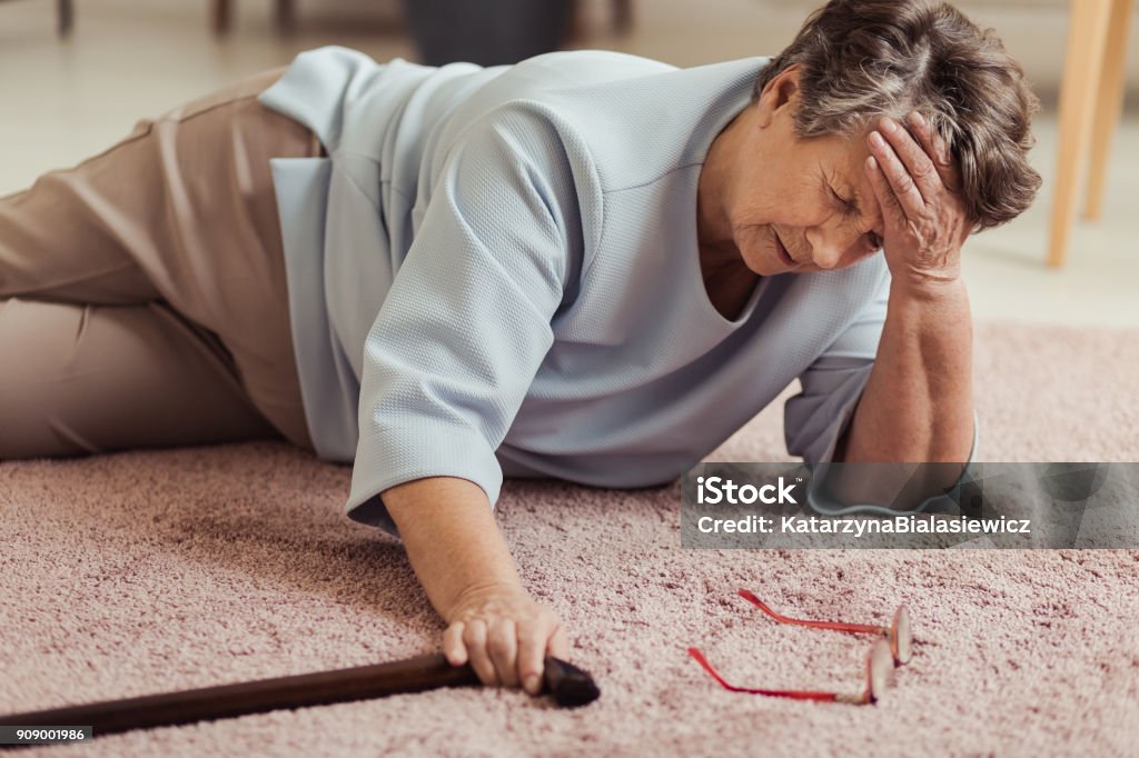 Sick senior woman with headache Sick senior woman with headache lying on the floor with wooden stick Falling Stock Photo