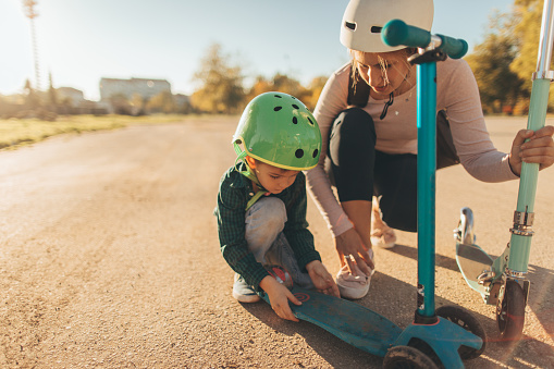 Photo of a little boy repairing broken push scooter with a little help from his mother