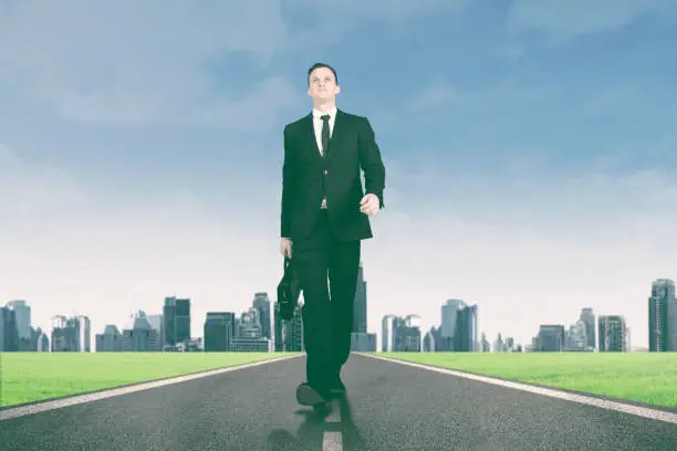 Portrait of male manager carrying a briefcase while walking on the road with city background