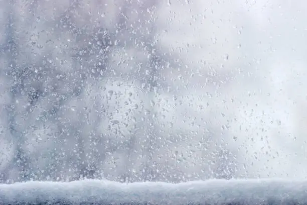 Background of the streams and drops of water on the window pane with accumulation of wet snow at the bottom of window during a snowfall