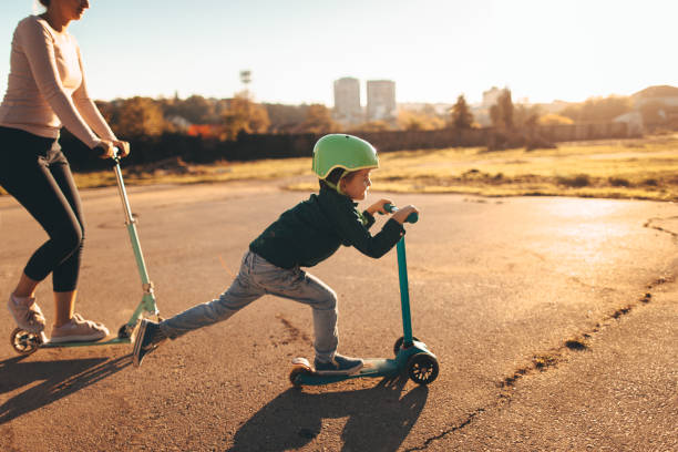 Little boy riding a push scooter with his mom Photo of a cheerful little boy riding a push scooter, with his mom right behind him push scooter stock pictures, royalty-free photos & images