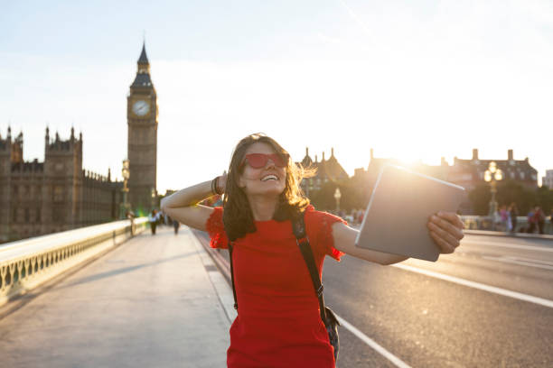 Woman taking selfie on street at sunset Cheerful tourist in red dress taking selfie with digital tablet on Westminister bridge. big ben stock pictures, royalty-free photos & images