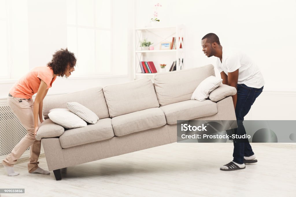 African-american couple placing sofa at new home Full length of happy black couple placing sofa in living room of new home. Moving, interior design and real estate concept, copy space New Stock Photo