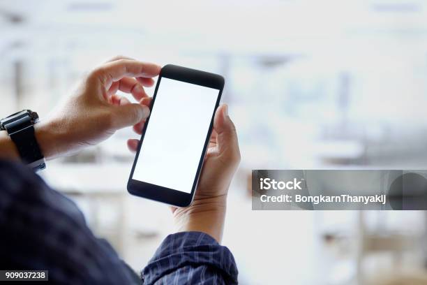 Mockup Image Of Man Hands Holding Black Mobile Phone With Blank White Screen In Office Stock Photo - Download Image Now