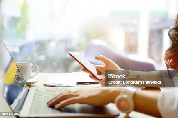 Young Woman Looking Smartphone And Using Laptop Computer While Working In Office Stock Photo - Download Image Now