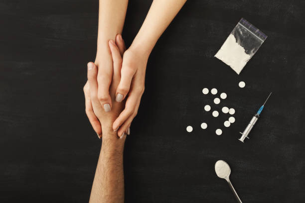 Drug addict hands on dark table Drug addict hands asking for help on dark table with cooked heroine, pills, spoon and plastic bag. Concept for drug addiction and International Day against Drug Abuse, top view morphine drug stock pictures, royalty-free photos & images