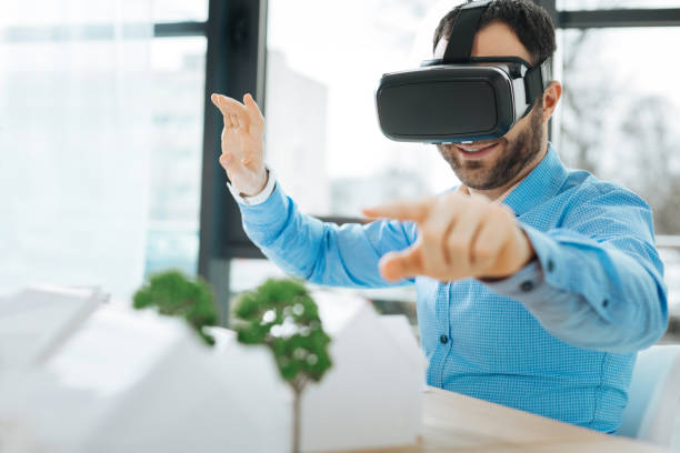 istock Smiling architect in VR headset pointing at house models 909042538
