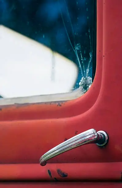 Side of red truck with broken window and chrome doorhandle - focus on doorhandle