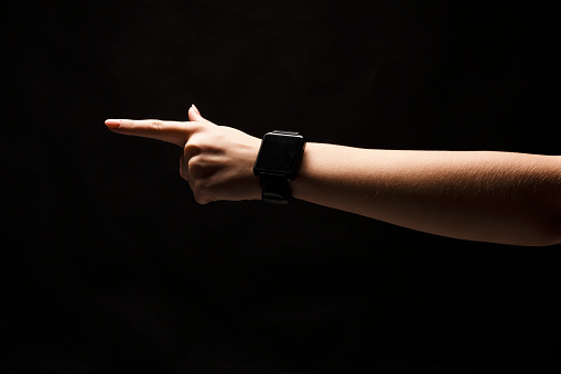 Female hand with smart watches, forefinger pointing away. Hand gestures - woman indicating on virtual object with index finger, isolated on black background, technology concept, copy space