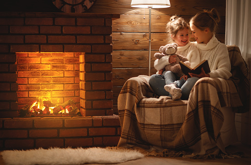 istock hija de madre y el niño familia feliz Lee libro en noche de invierno junto a la chimenea 909044860