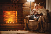 happy family mother and child daughter read book on winter evening near fireplace