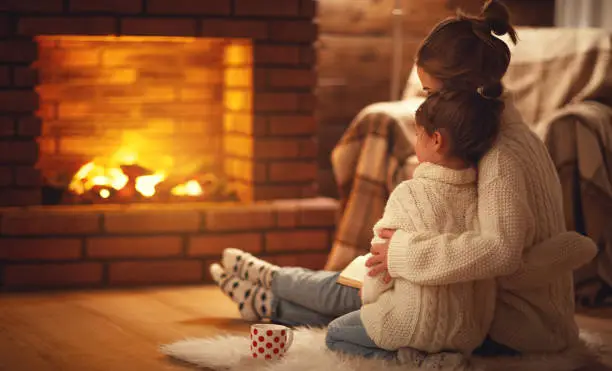 Photo of family mother and child hugs and warm on winter evening by fireplace