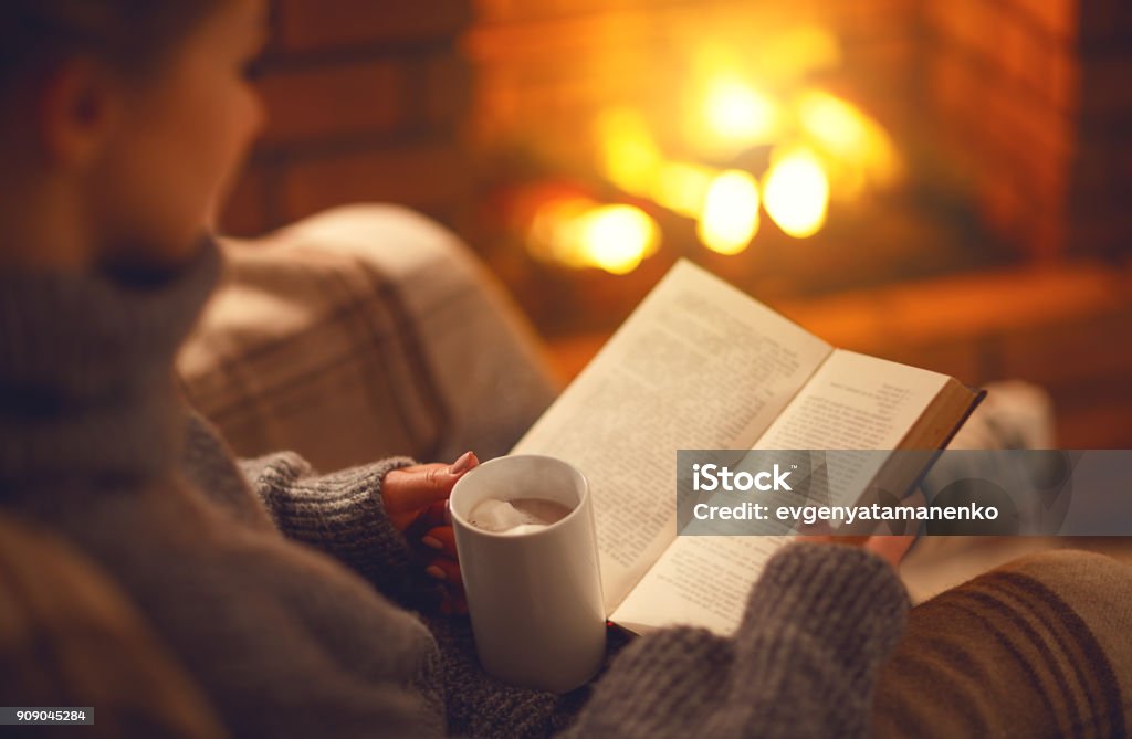 libro y taza de café en manos de la niña en la noche de invierno junto a la chimenea - Foto de stock de Leer libre de derechos