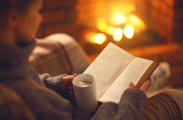 libro y taza de café en manos de la niña en la noche de invierno junto a la chimenea - reading a book fotografías e imágenes de stock