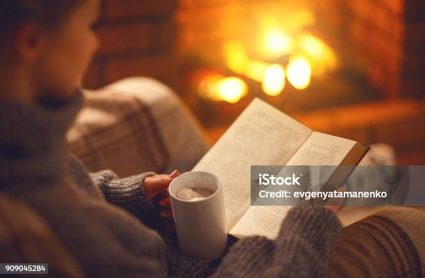Libro Y Taza De Café En Manos De La Niña En La Noche De Invierno Junto A La Chimenea Foto de stock y más banco de imágenes de Leer