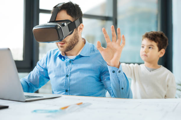 istock Little boy touching back of father testing VR headset 909049212