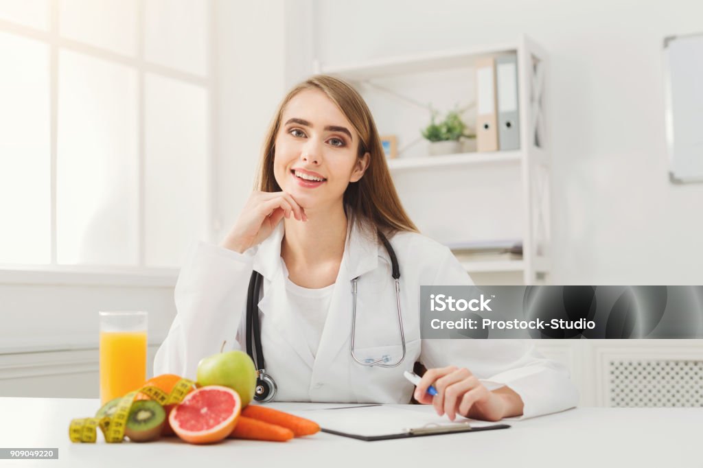 Nutritionist desk with fruit and measuring tape Nutritionist desk with healthy fruits, juice and measuring tape. Dietitian working on diet plan at office, smiling at camera. Weight loss and right nutrition concept Nutritionist Stock Photo