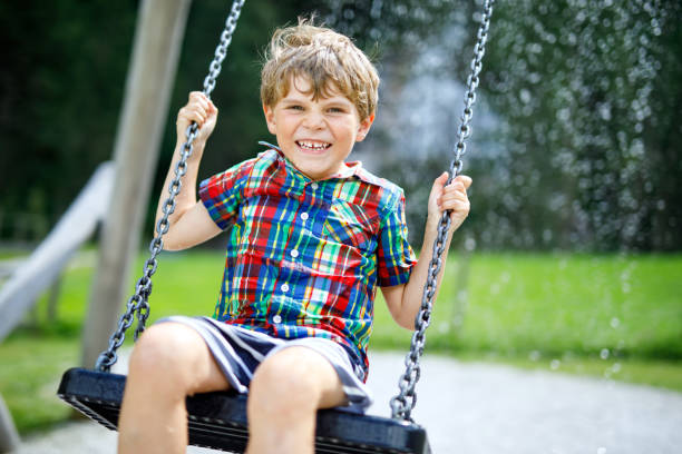 istock Funny kid boy having fun with chain swing on outdoor playground during rain 909061284