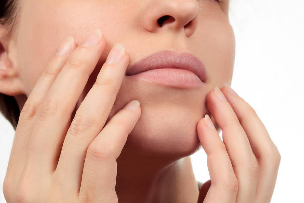 istock Healthy lips closeup without makeup. Hands show beautiful closed mouth without lipstick. Nails without nail-varnish polish. Beauty. Face without cosmetics on white background. 909062012