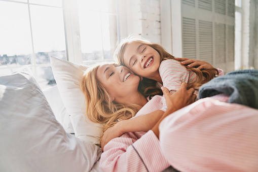Young beautiful mother with her cute little daughter smiling while lying on the bed at home