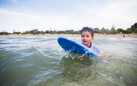 Kid on surfboard on beach enjoying outdoors at long bay, Auckland, New Zealand.
