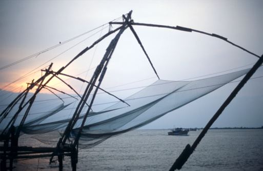 Picture shows the sunset at the seaside. In the foreground are fishing nets, in the background sky and cutters. Kochi, India.